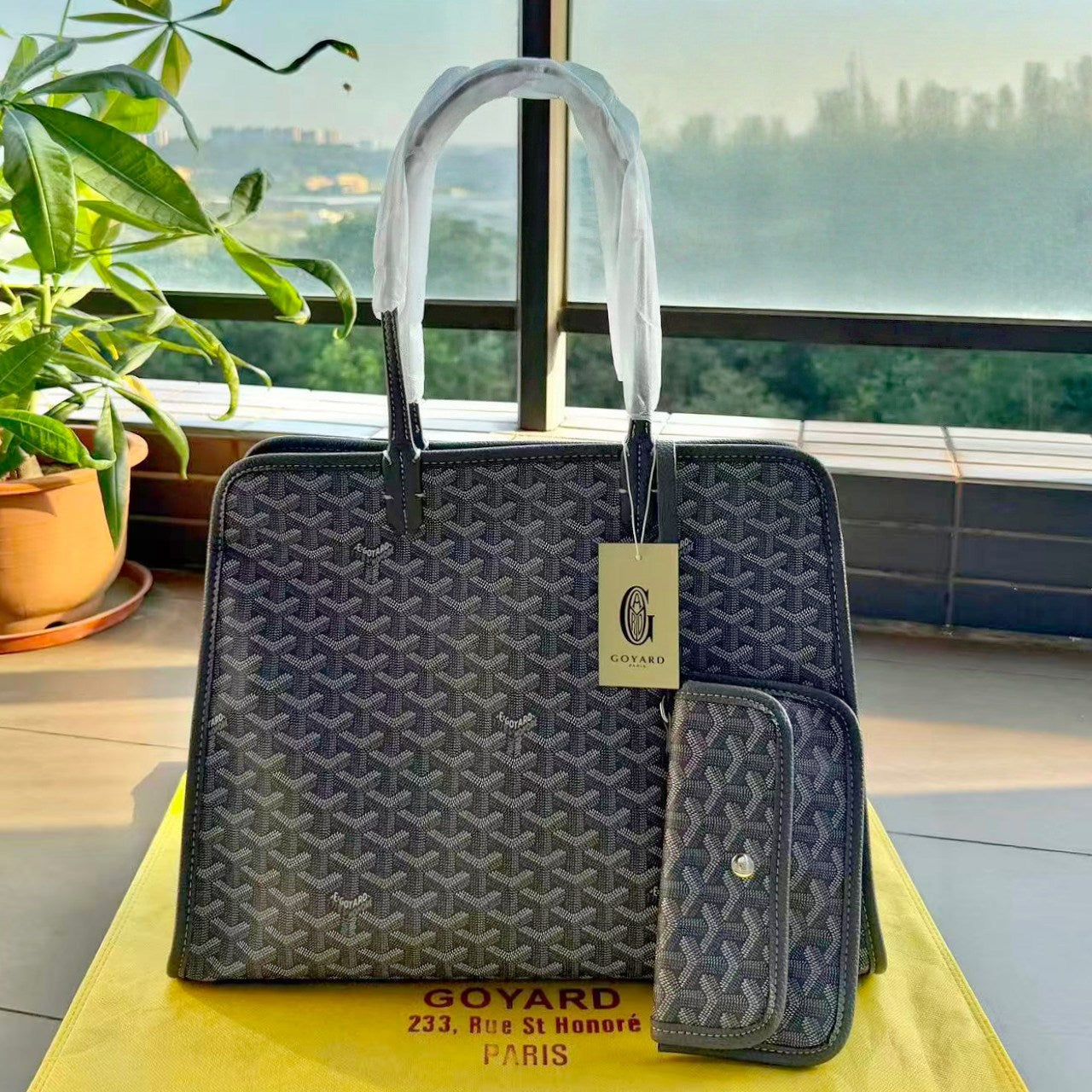 Goyard handbag with a matching wallet on a yellow surface with a blurred cityscape in the background.