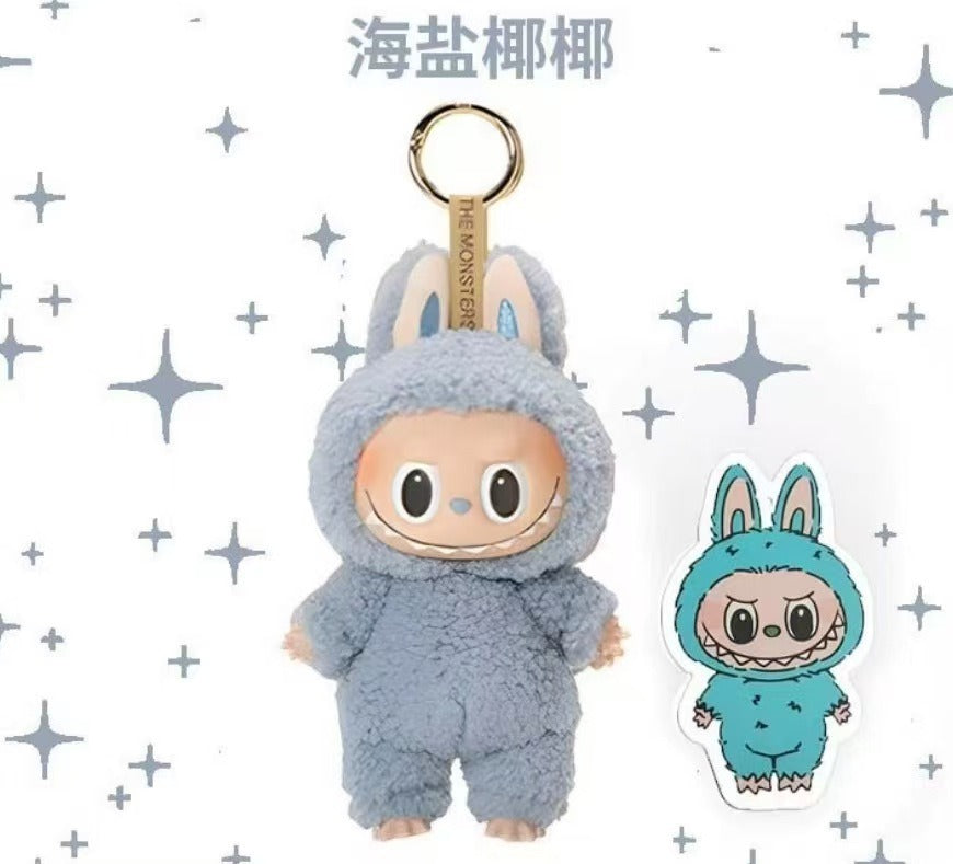 A plush character keychain in a fuzzy light blue bunny suit with a gold key ring, shown alongside a matching die-cut sticker on a white background with gray star graphics. Chinese text appears at the top.
