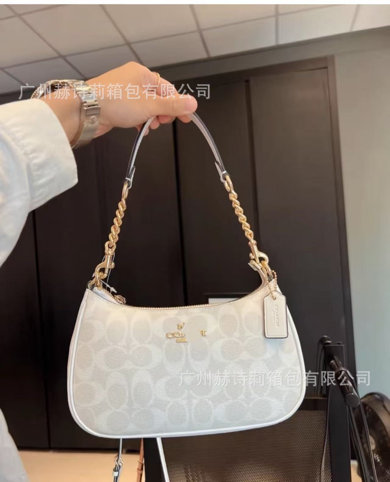 White handbag with gold chain handle held by a person indoors.