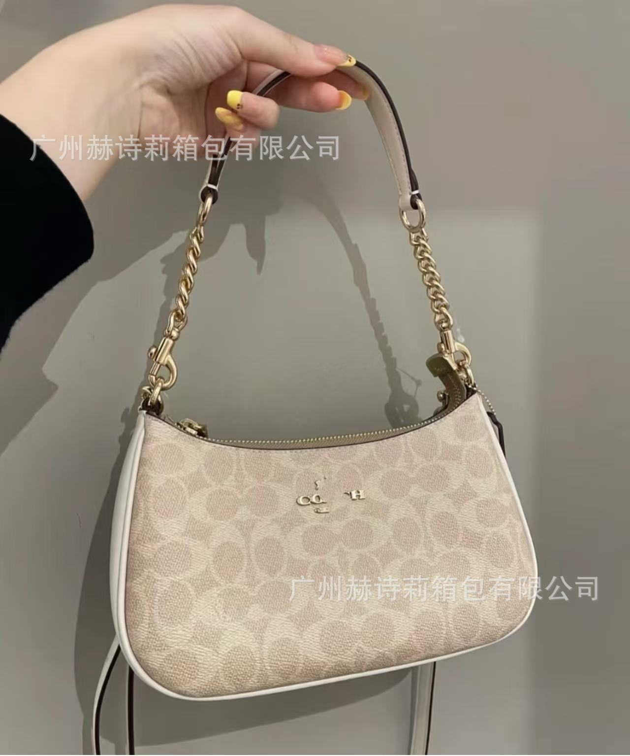Beige handbag with gold chain handle held by a hand against a gray background