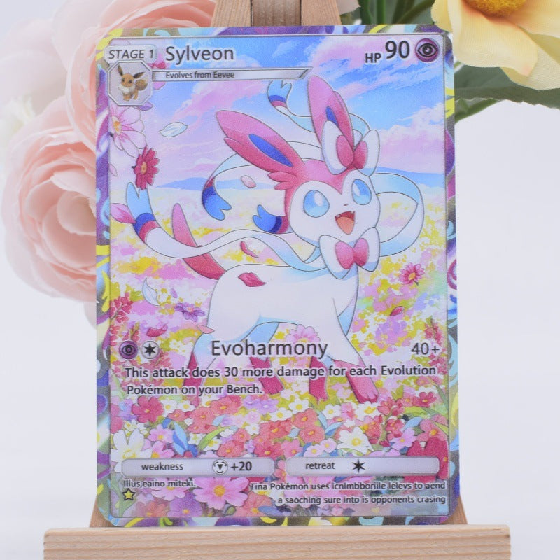 A holographic Pokémon trading card featuring Sylveon, displayed on a small wooden stand with soft pink and yellow flowers in the background.