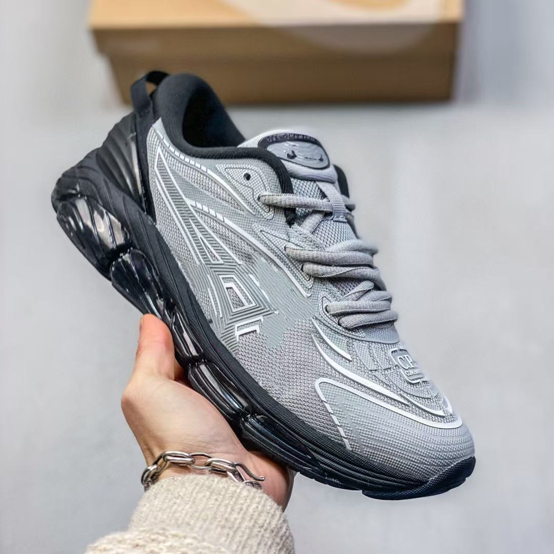 Gray athletic shoe with black sole held by a hand against a neutral background