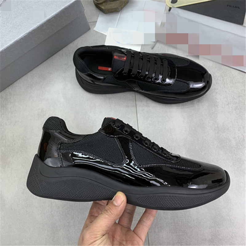 Black glossy sneakers held by a hand on a light gray floor.