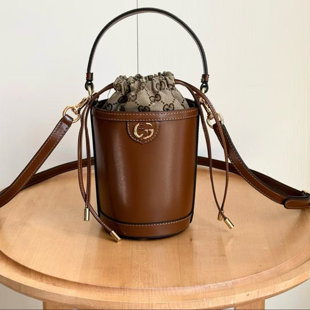 A brown leather bucket bag with a drawstring top, gold-tone hardware, and a Gucci monogram pattern lining, displayed on a round wooden table. Chinese text in the top left corner shows the style number 760201 and dimensions 11.