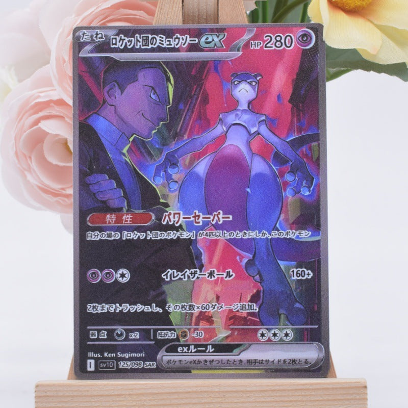 A Japanese Pokémon trading card featuring Mew and a man, displayed on a small wooden stand with soft pink and yellow flowers blurred in the background.