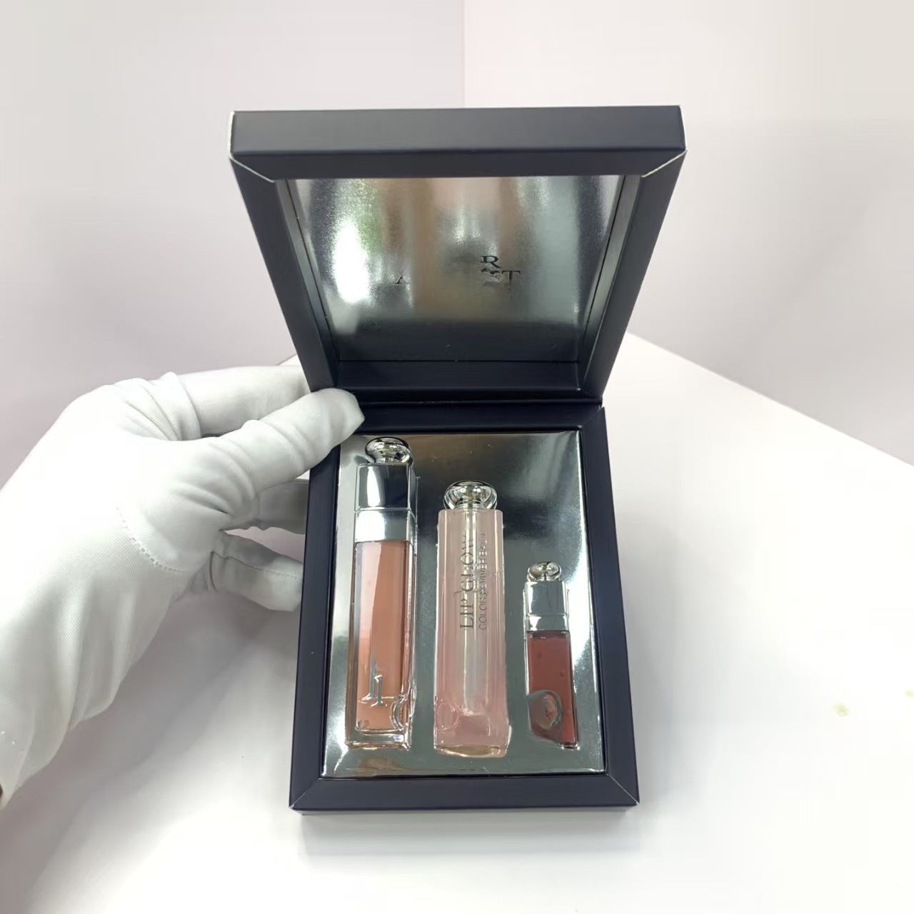 Lip gloss set in a black box held by a gloved hand on a white background