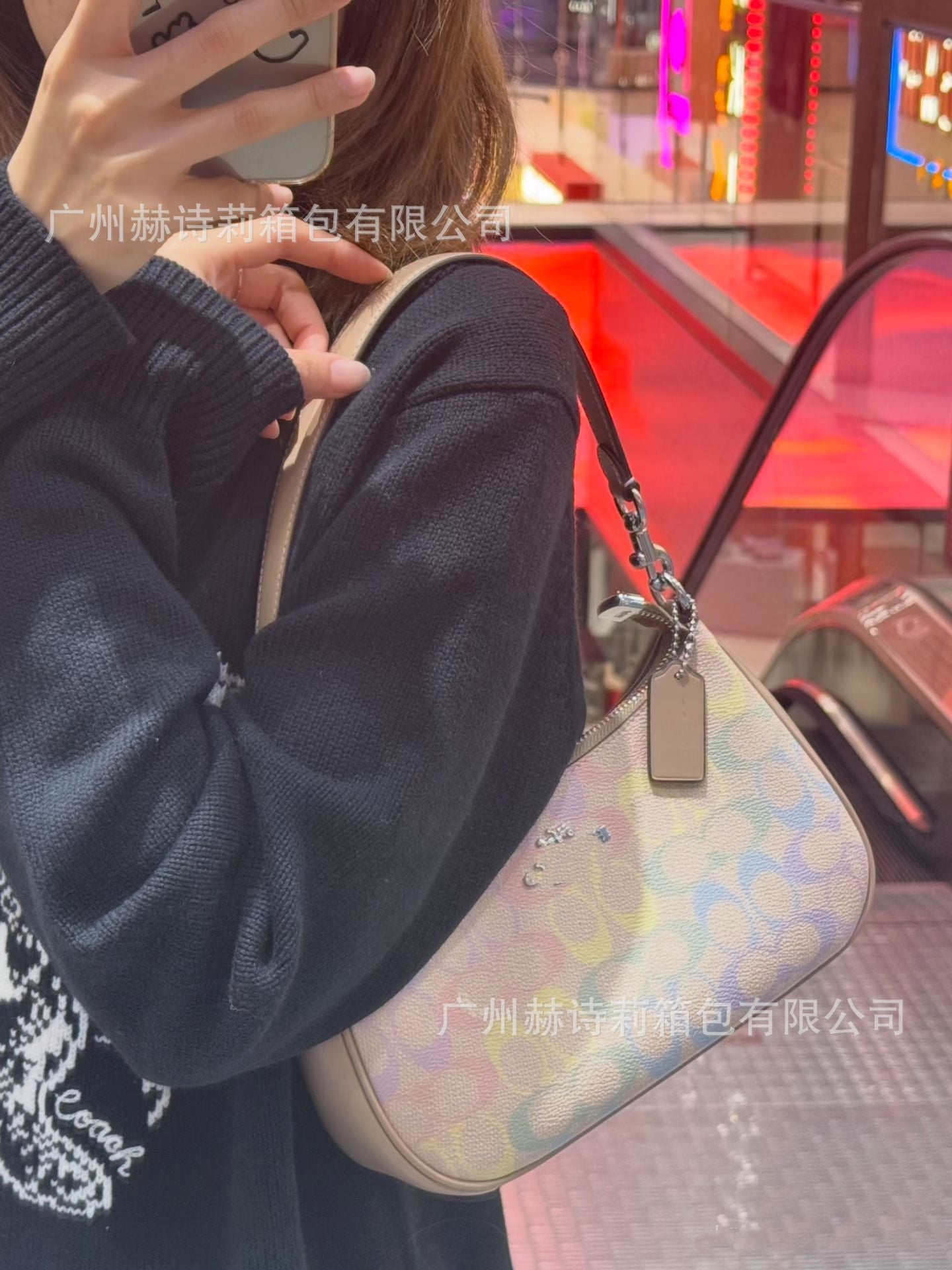 Person holding a Coach handbag with a colorful pattern in an urban setting