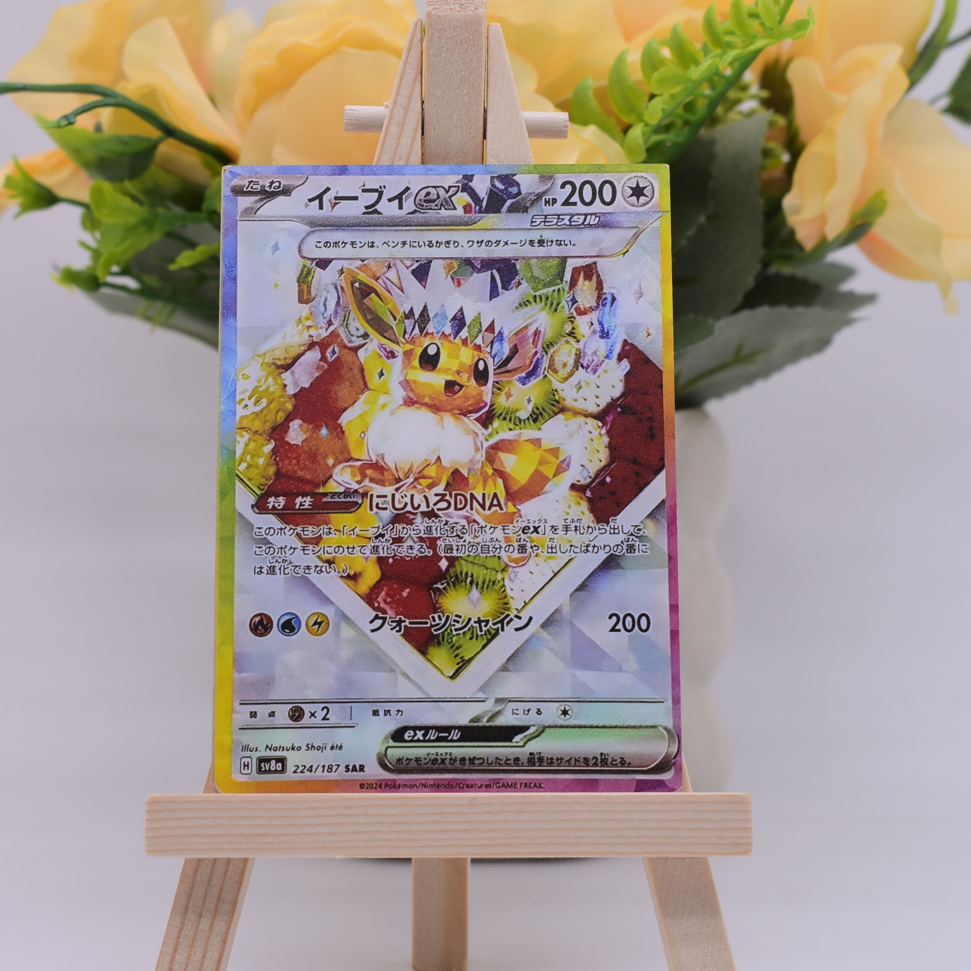 A Pokémon TCG card featuring Eevee, displayed upright on a small wooden easel with blurred yellow flowers in the background.