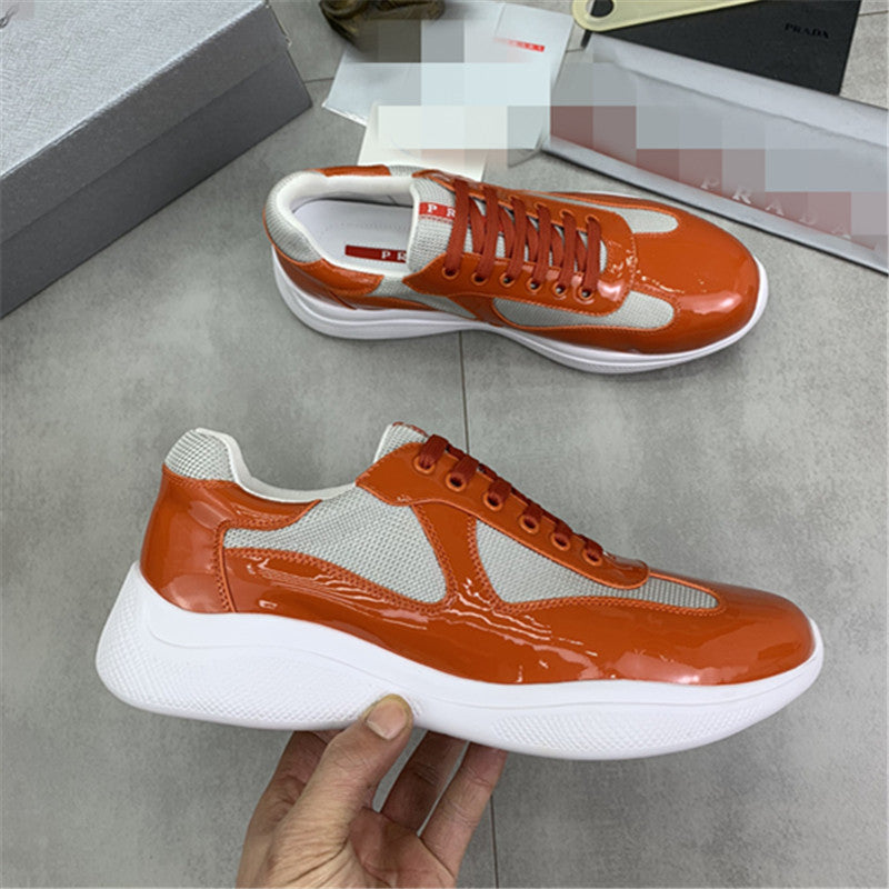 Orange and white sneakers held by a hand on a gray floor.