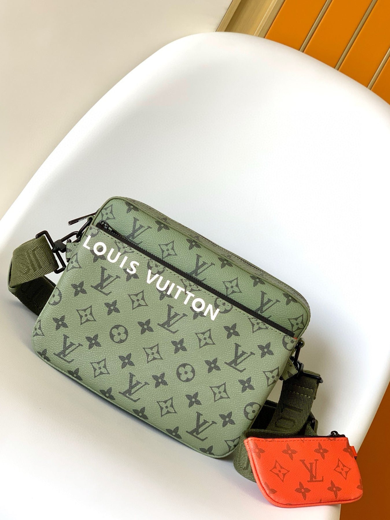 Green Louis Vuitton bag with a red pouch on a white surface