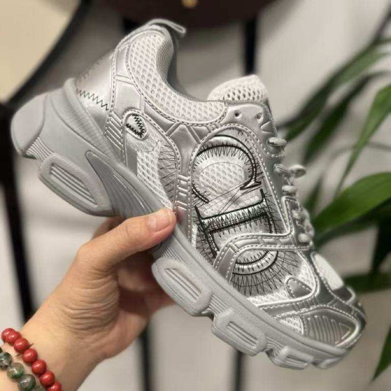 Silver sneaker with intricate design held by a hand against a neutral background