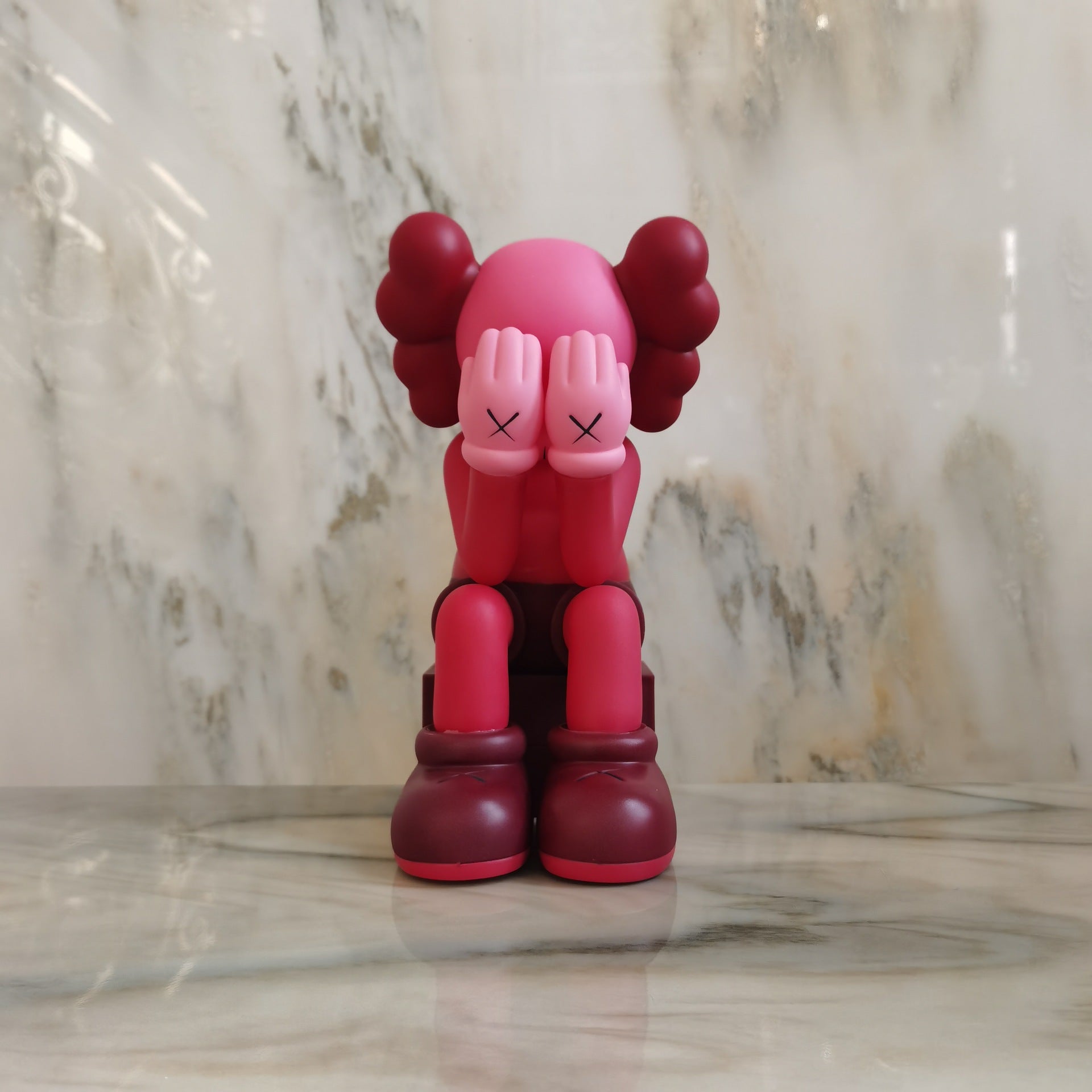 A pink and red cartoon-style collectible figure with eyes closed, sitting on a marble surface against a marble background.