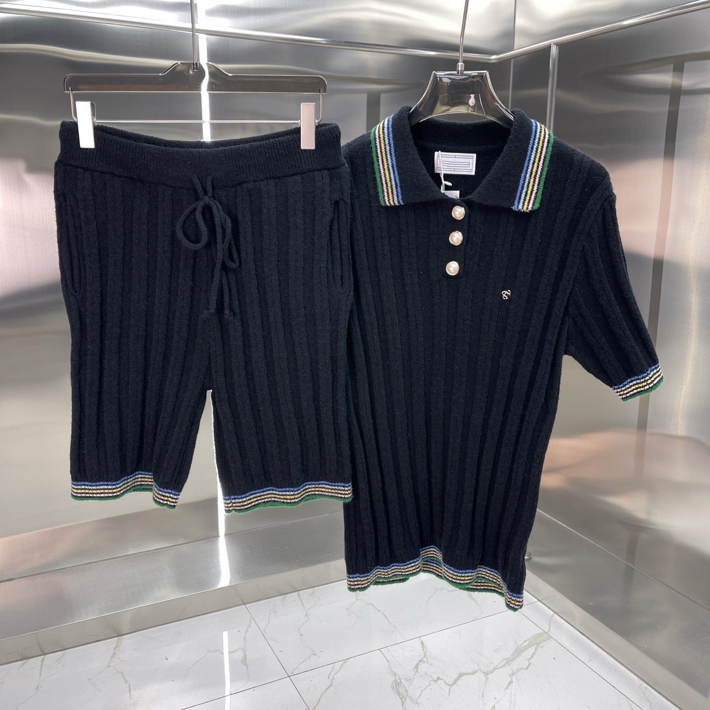 Navy blue ribbed knit polo shirt and shorts set on hangers against a reflective metallic wall.