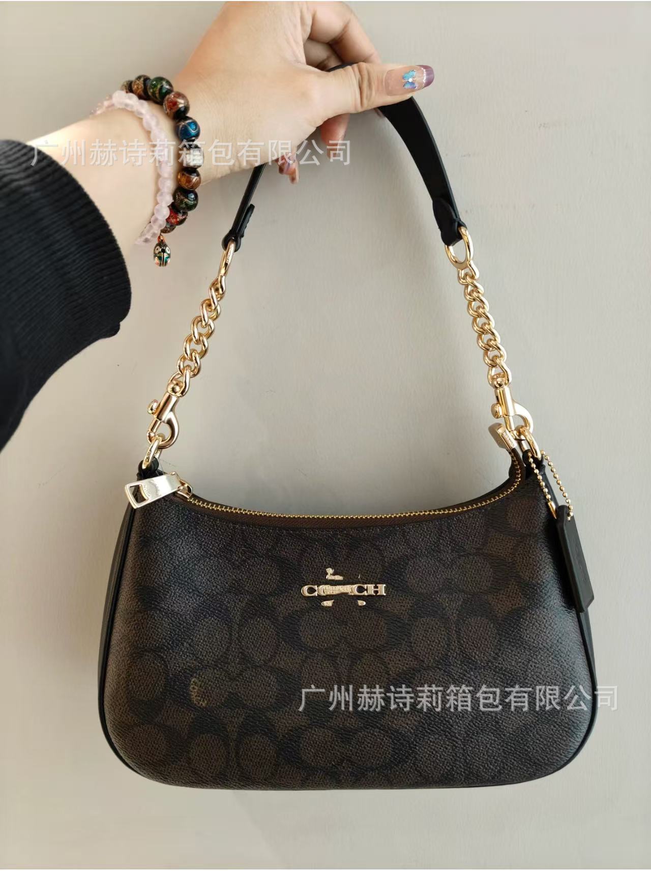 Black handbag with gold chain handle held by a person against a neutral background