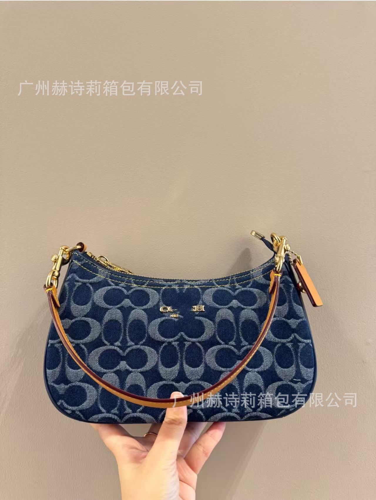 Blue handbag with brown handle held against a beige background