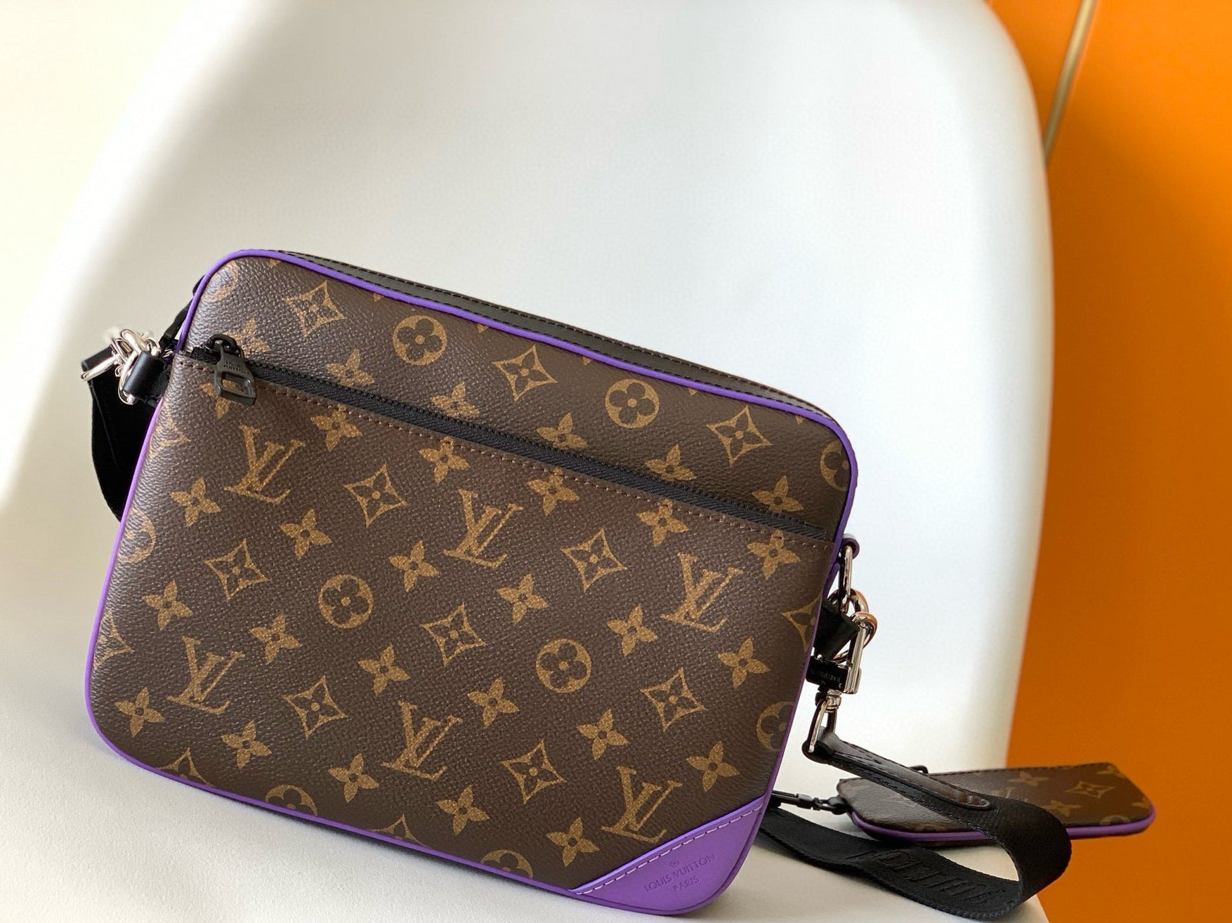 Designer handbag with monogram pattern and purple accents on a white and orange background