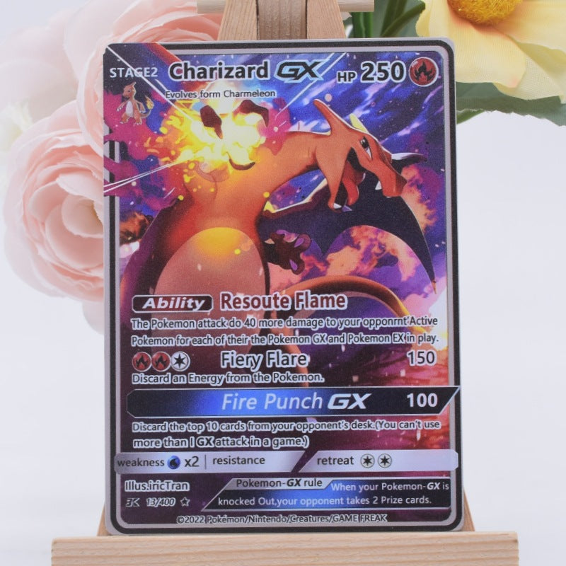 A Charizard GX Pokémon trading card displayed upright on a small wooden stand, with soft pink flowers and a yellow flower blurred in the background.