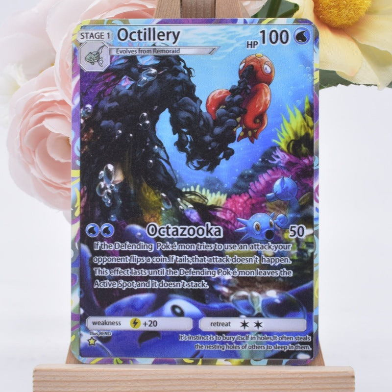 A Pokémon trading card featuring Octillery, displayed upright on a small wooden stand with soft pink and yellow flowers blurred in the background.