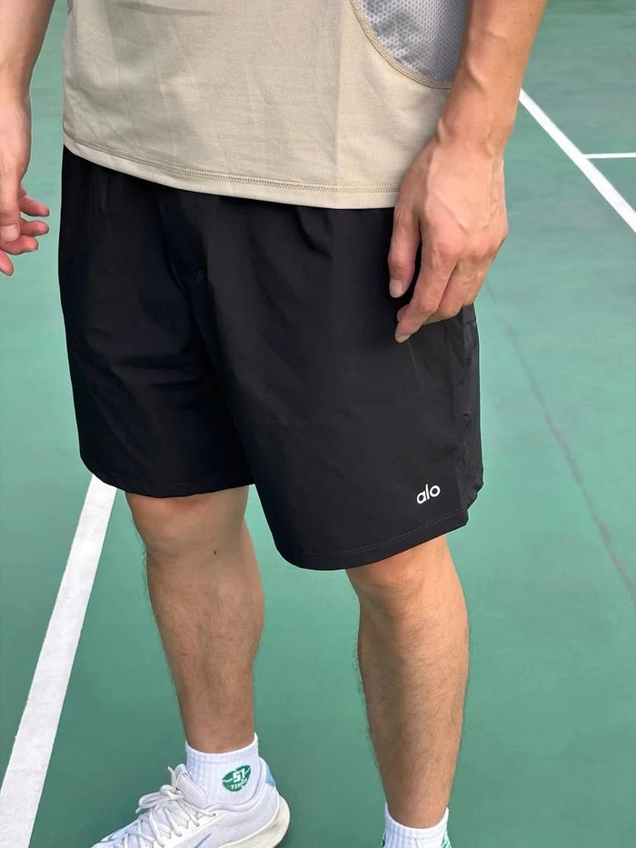 Person wearing black shorts with a logo on a tennis court