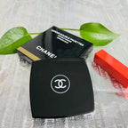 Chanel makeup compact with green leaves and a red object in the background