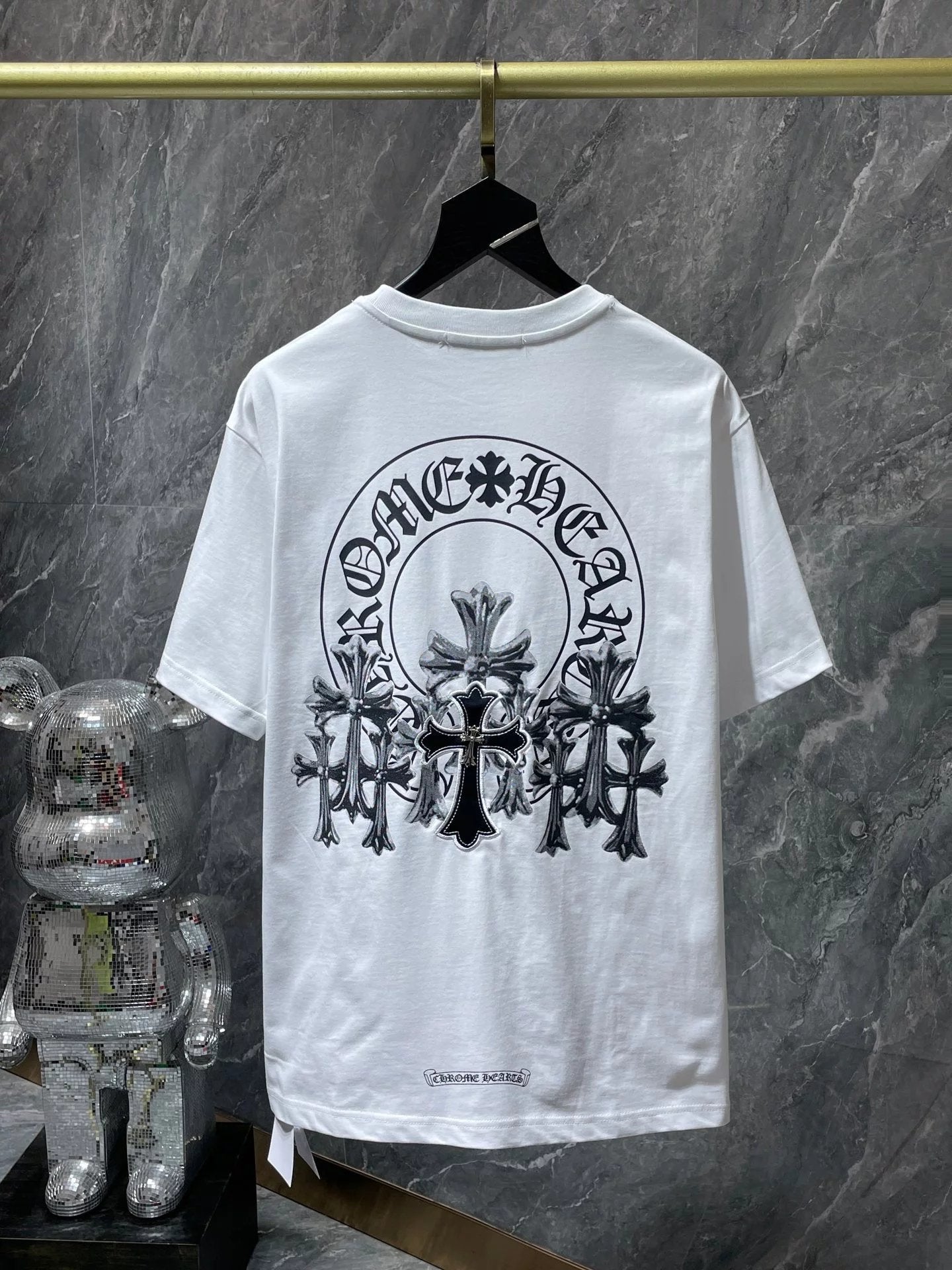 White t-shirt with black graphic design on a hanger against a marble wall.