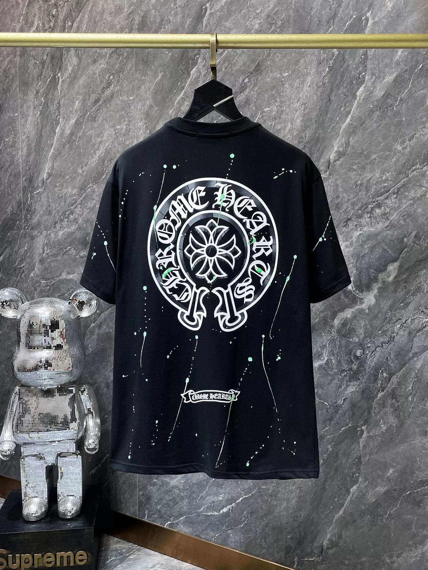 Black t-shirt with white graphic design on a hanger against a gray marble wall.