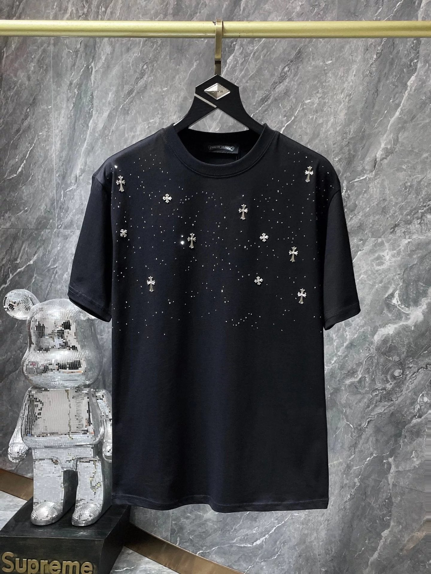 Black t-shirt with white cross patterns on a hanger against a marble wall.