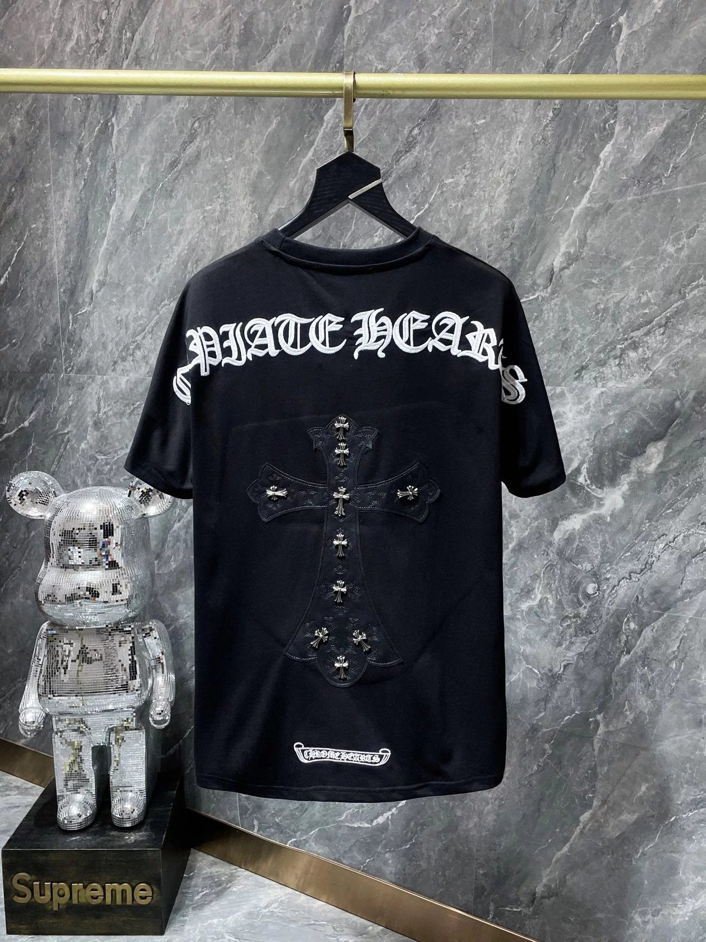 Black t-shirt with white text on a hanger against a gray marble background, next to a decorative figure and Supreme box.
