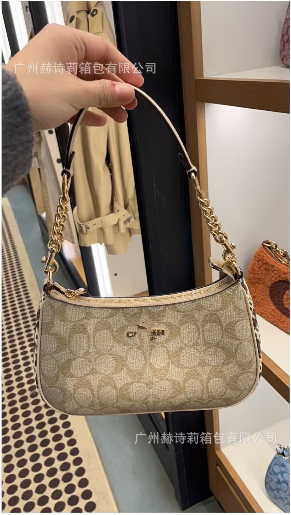 Beige handbag with gold chain held by a hand, blurred background