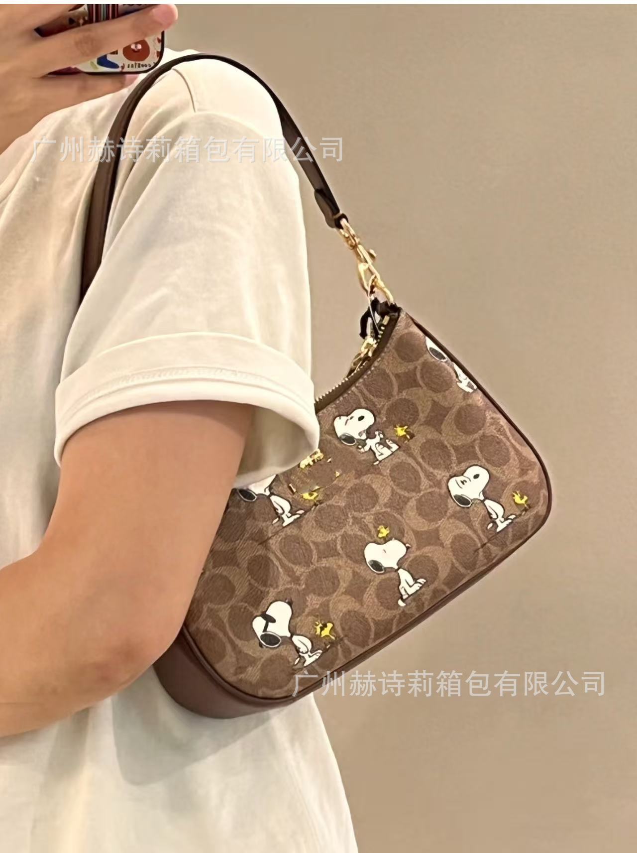 Brown handbag with Snoopy design held by a person wearing a white shirt.