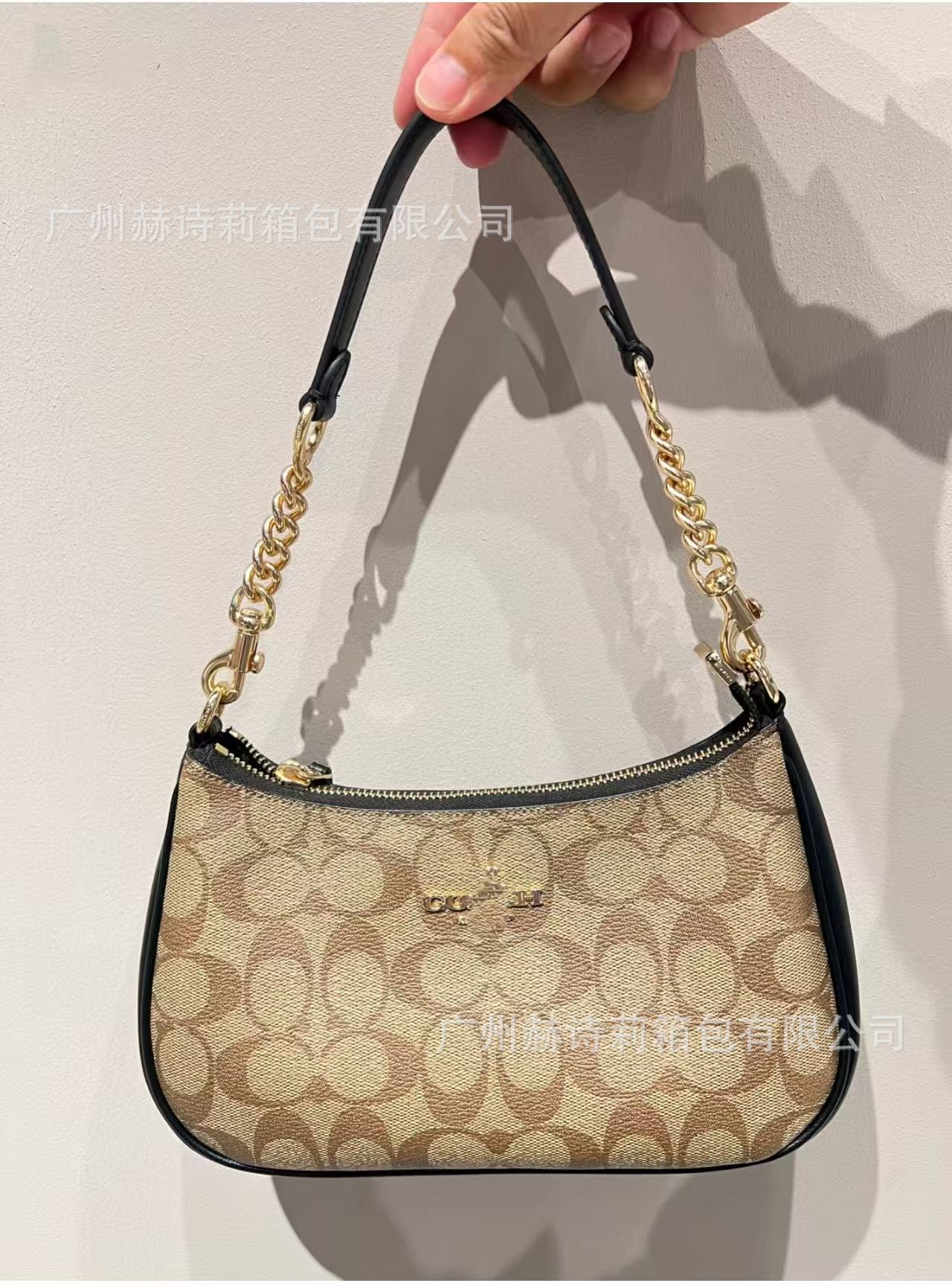 Handbag with chain detail held by a hand against a plain background