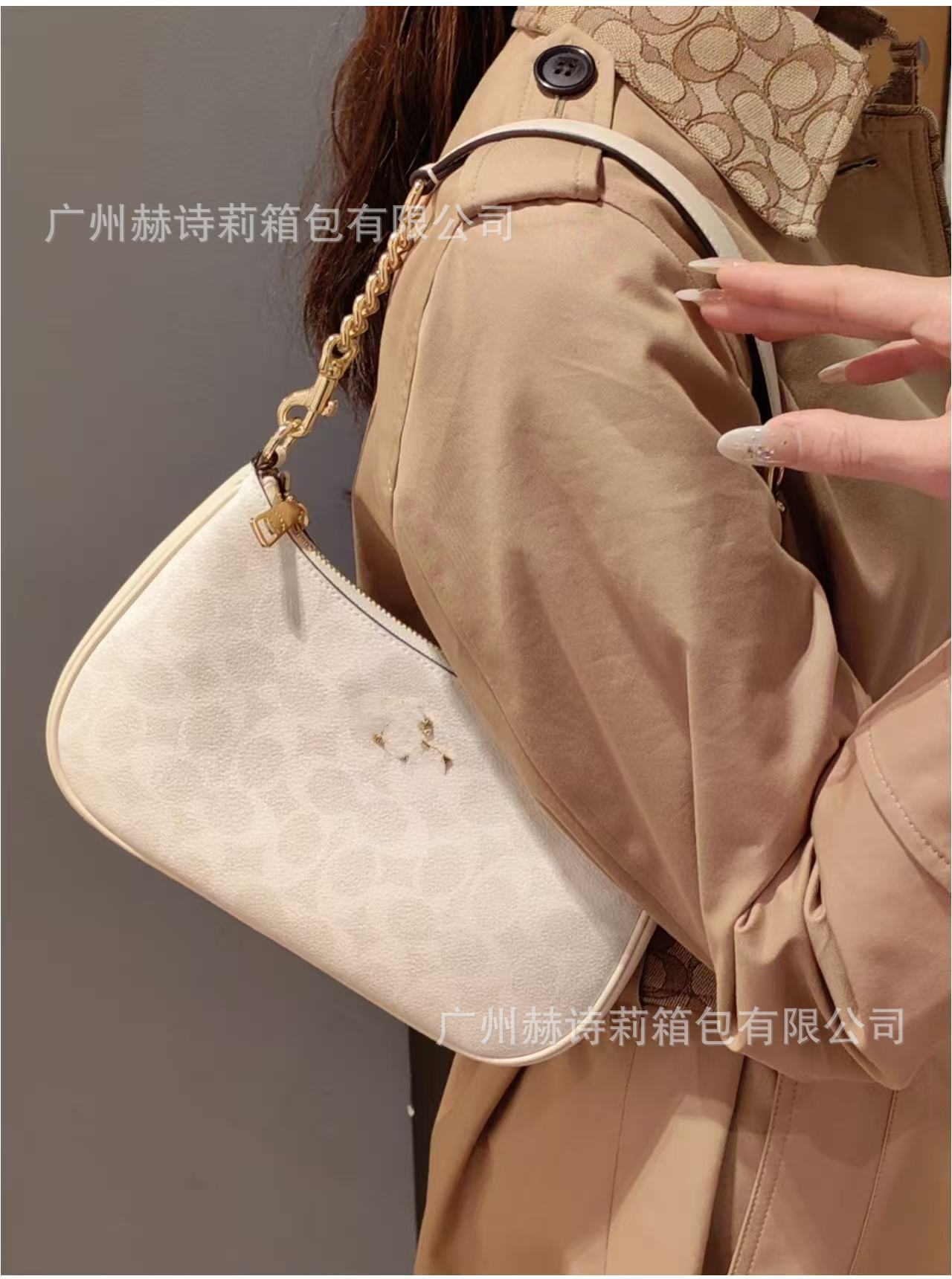 Beige handbag held by a person wearing a beige coat against a gray background