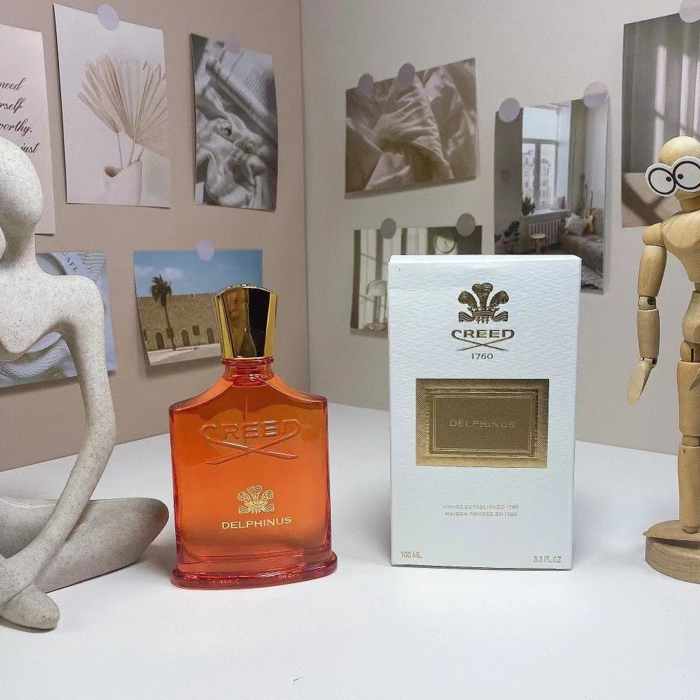Creed Delphines perfume bottle and packaging on a white surface with decorative items in the background.
