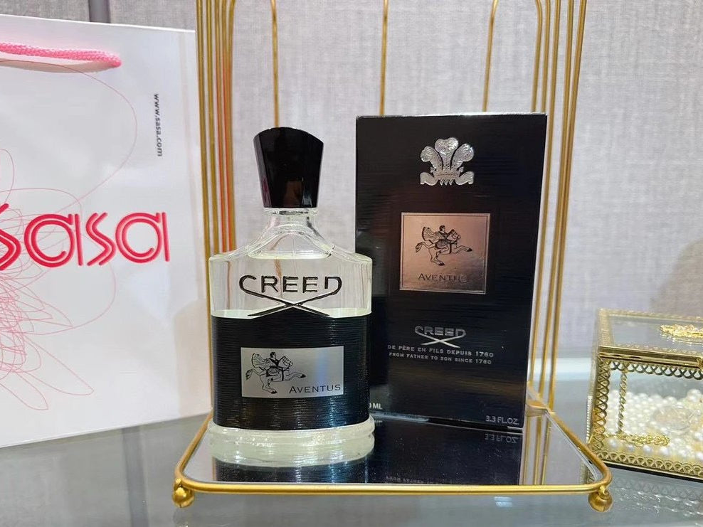 Creed perfume bottle and packaging on a reflective surface with 'Sasa' branding in the background.