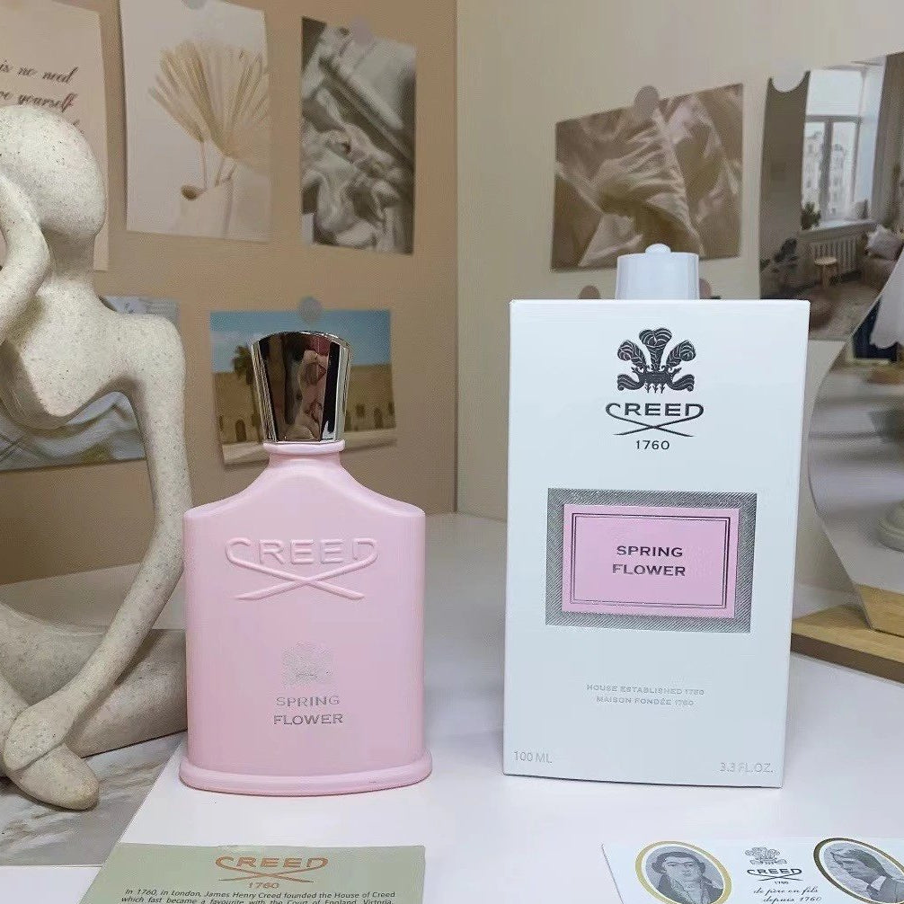 Pink Creed Spring Flower perfume bottle and packaging on a table with decorative items.