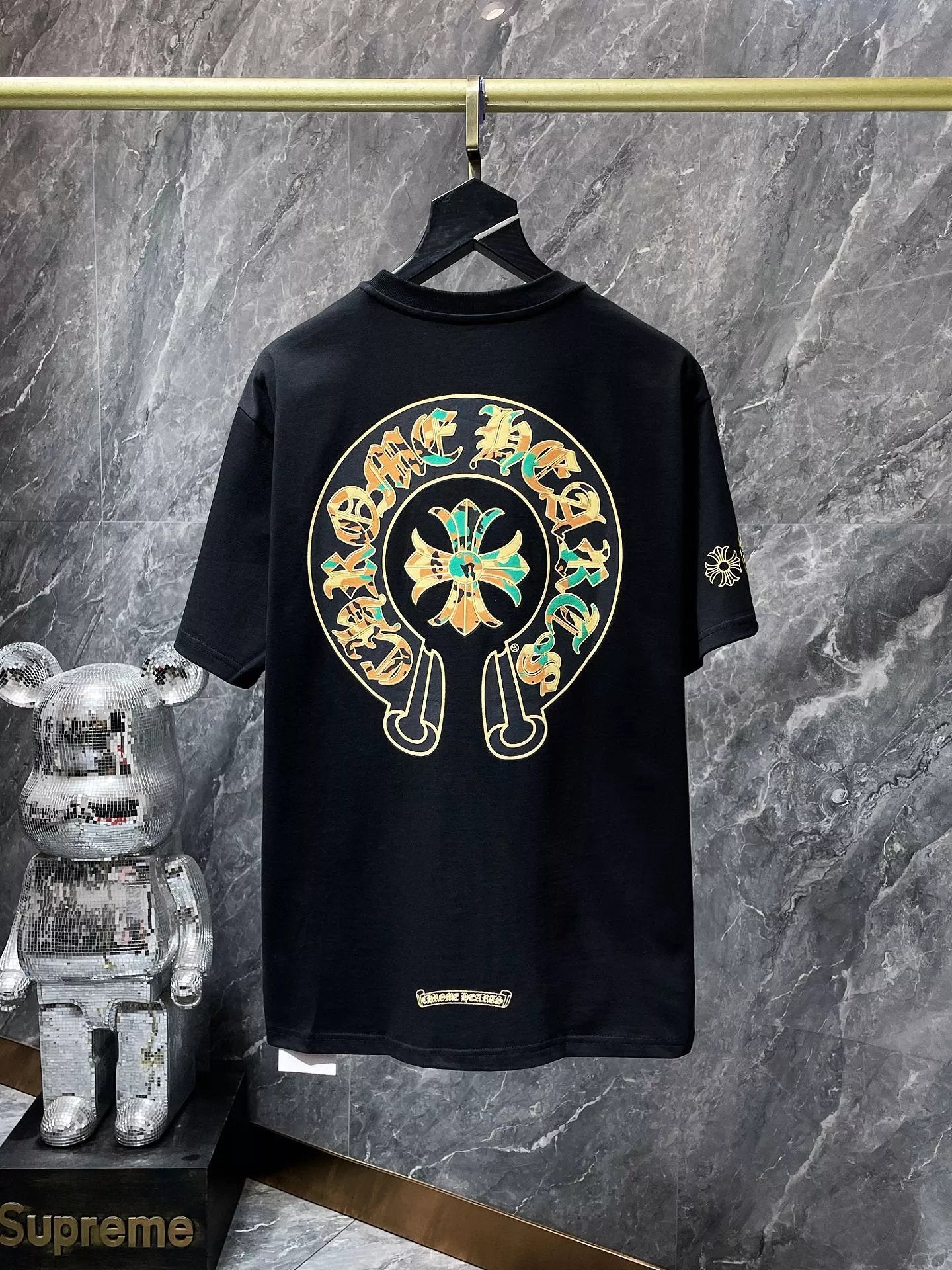 Black t-shirt with a colorful logo on a hanger against a marble wall.
