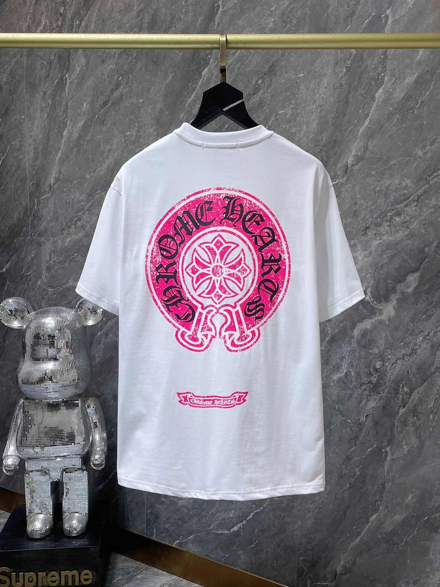 White t-shirt with pink graphic design on a hanger against a gray marble wall.