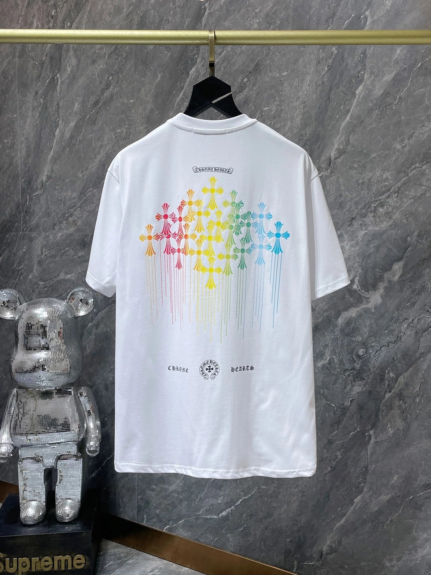 White t-shirt with colorful graphic design on a hanger against a gray marble wall.