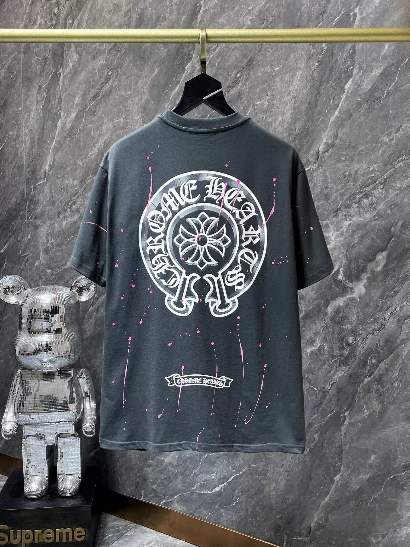 Black t-shirt with white graphic design on a hanger against a marble wall.