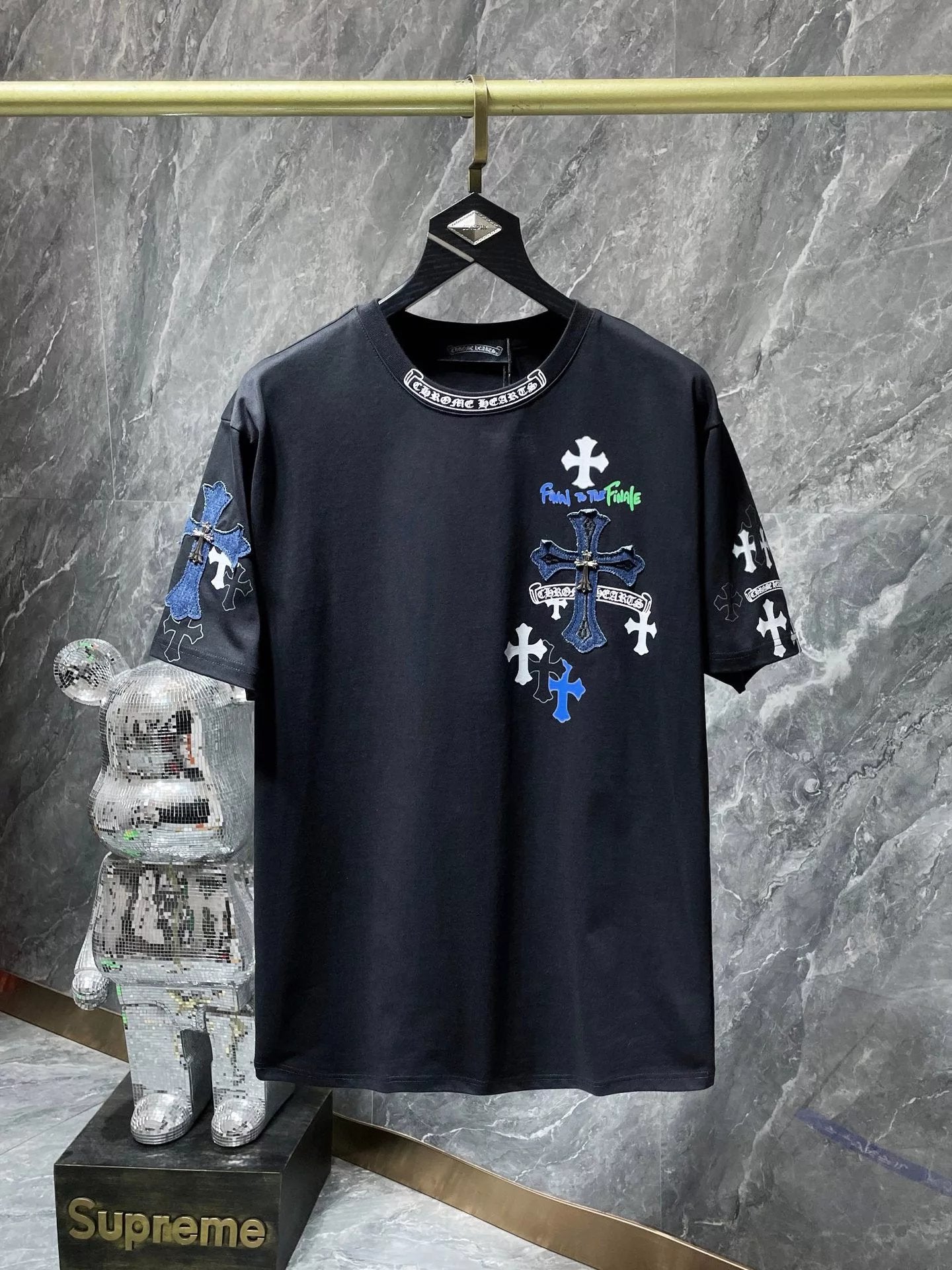Black t-shirt with colorful designs on a hanger against a marble wall.