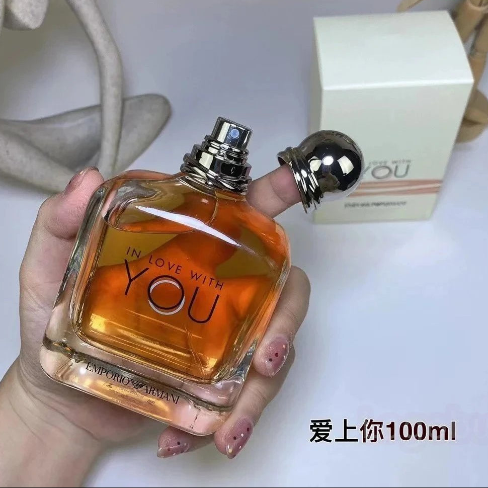 Perfume bottle labeled 'In Love with You' held by a hand, with packaging in the background.