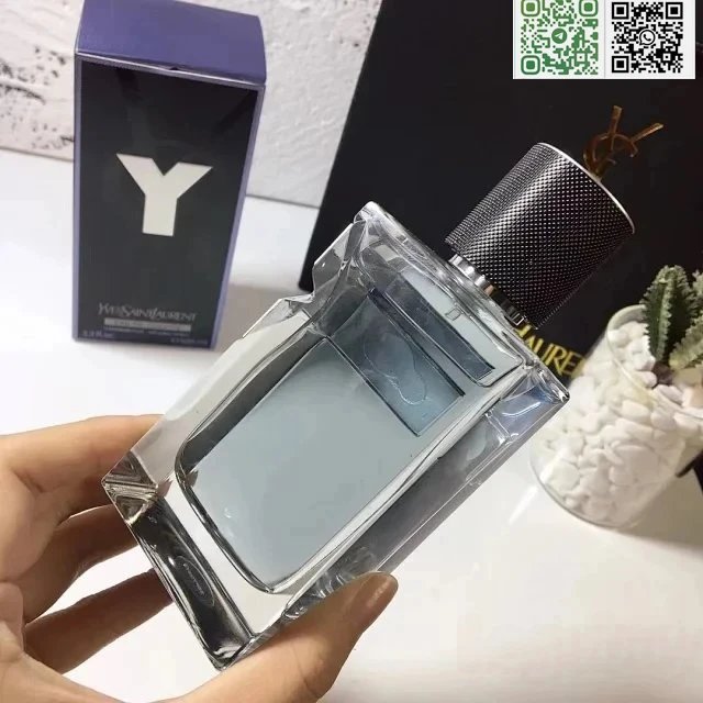 Hand holding a silver and black perfume bottle with 'Y' branding in the background.