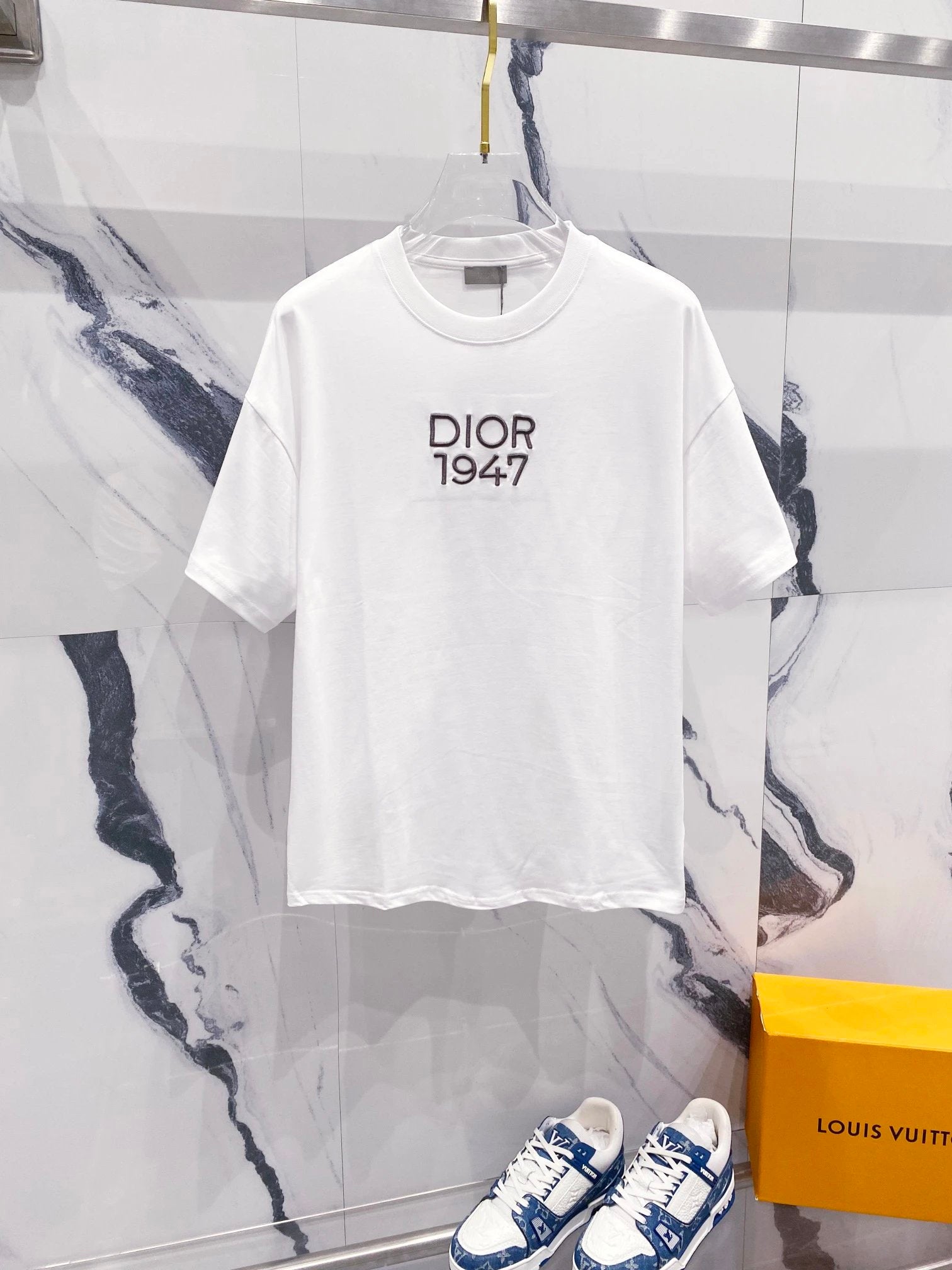 White t-shirt with 'Dior 1947' text on a marble surface with a Louis Vuitton box.