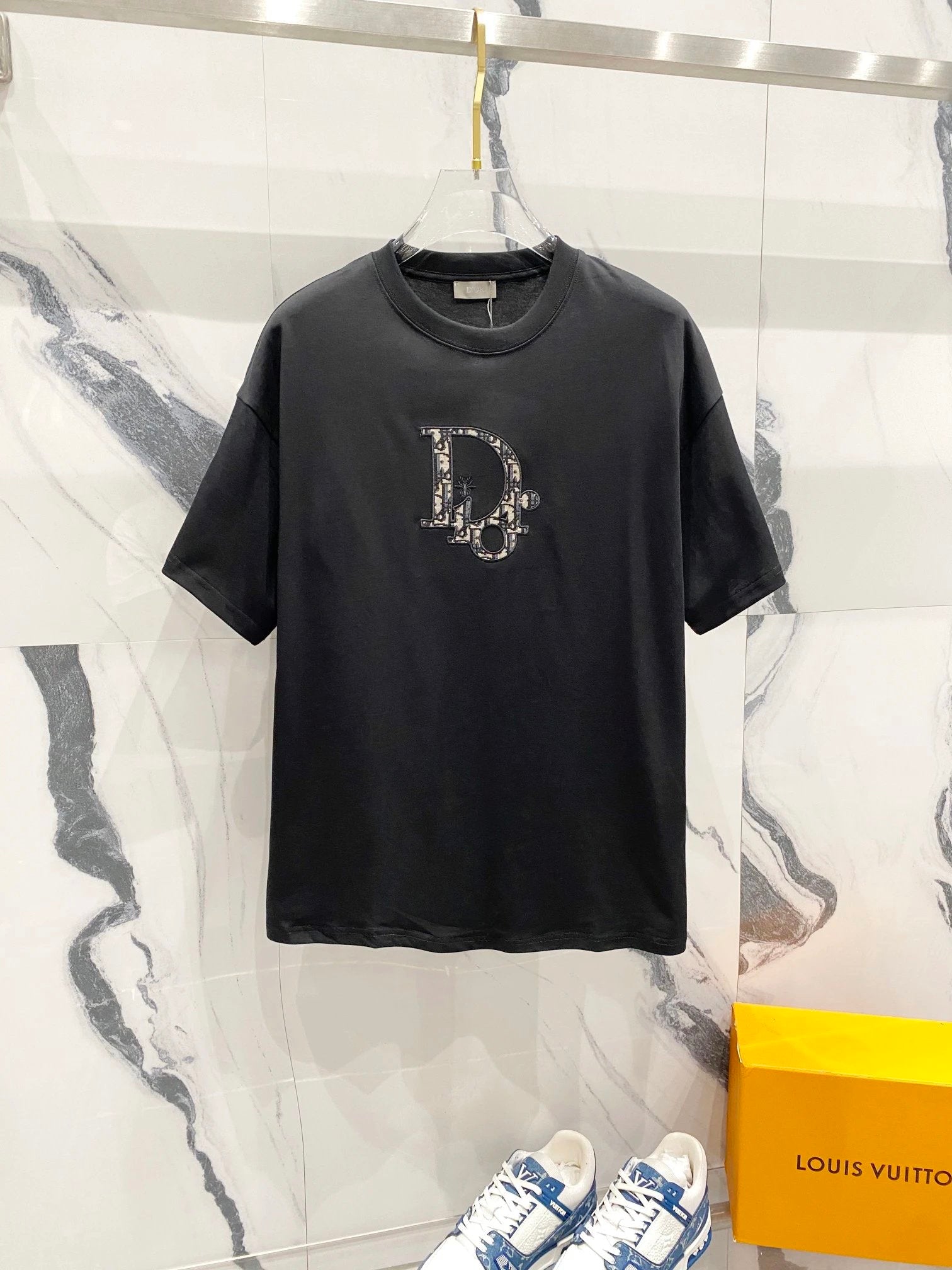 Black t-shirt with a logo on a marble surface next to a Louis Vuitton box.