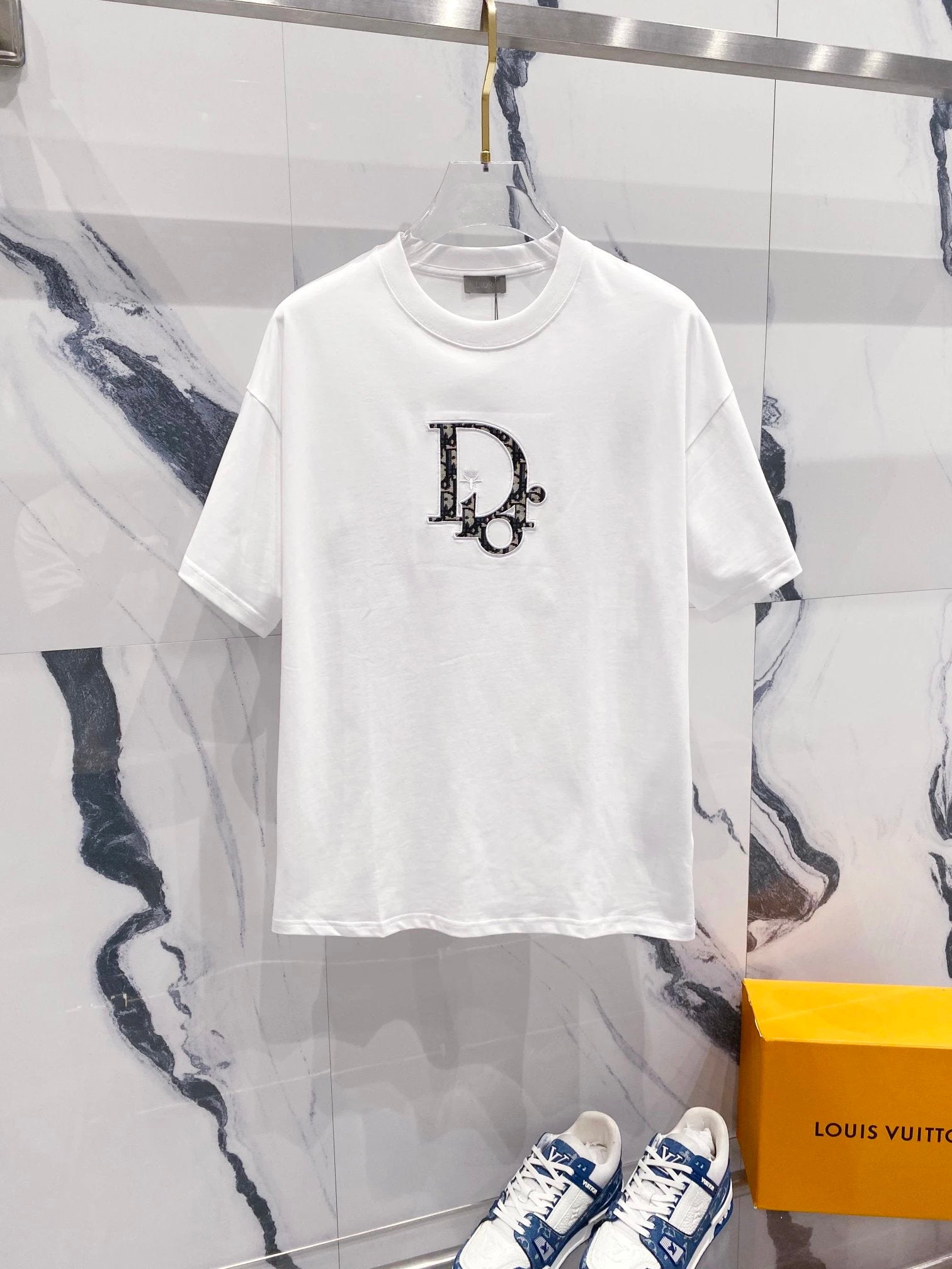 White t-shirt with a logo design on a marble surface with a Louis Vuitton box.