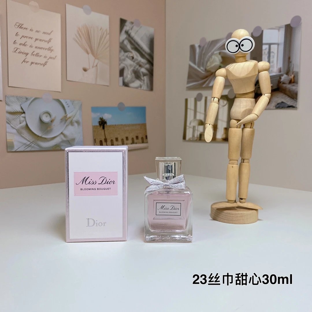 Dior perfume bottle and packaging on a table with a wooden mannequin and photos in the background.