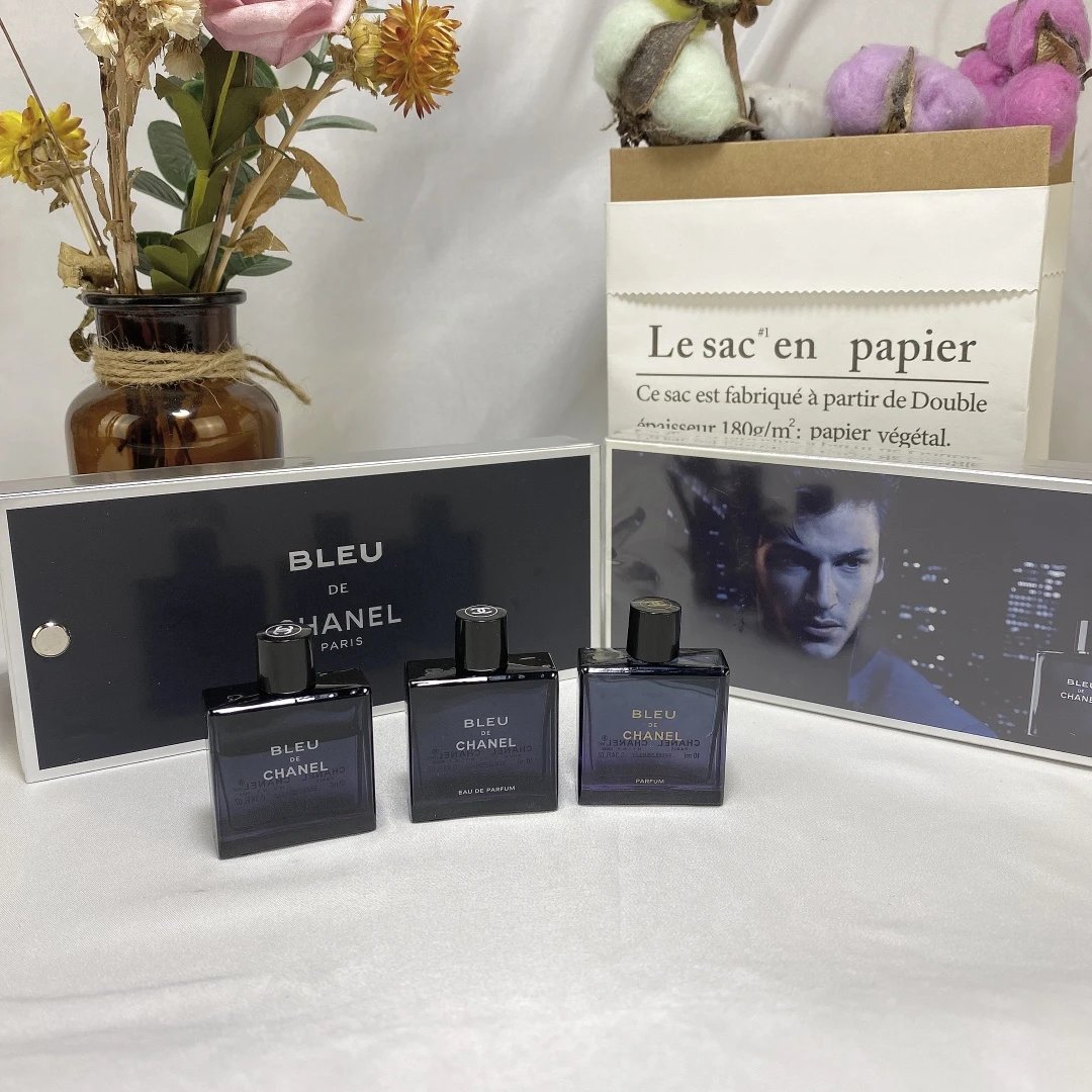 Three Chanel Bleu perfume bottles on a white surface with a magazine and decorative items in the background.