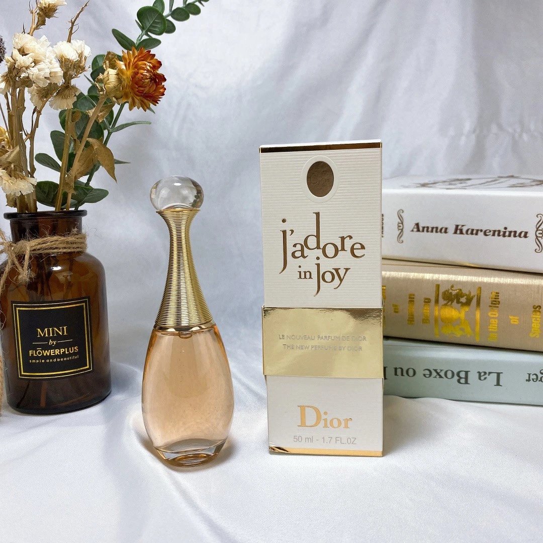 Dior Jadore perfume bottle and packaging on a white surface with books and flowers.