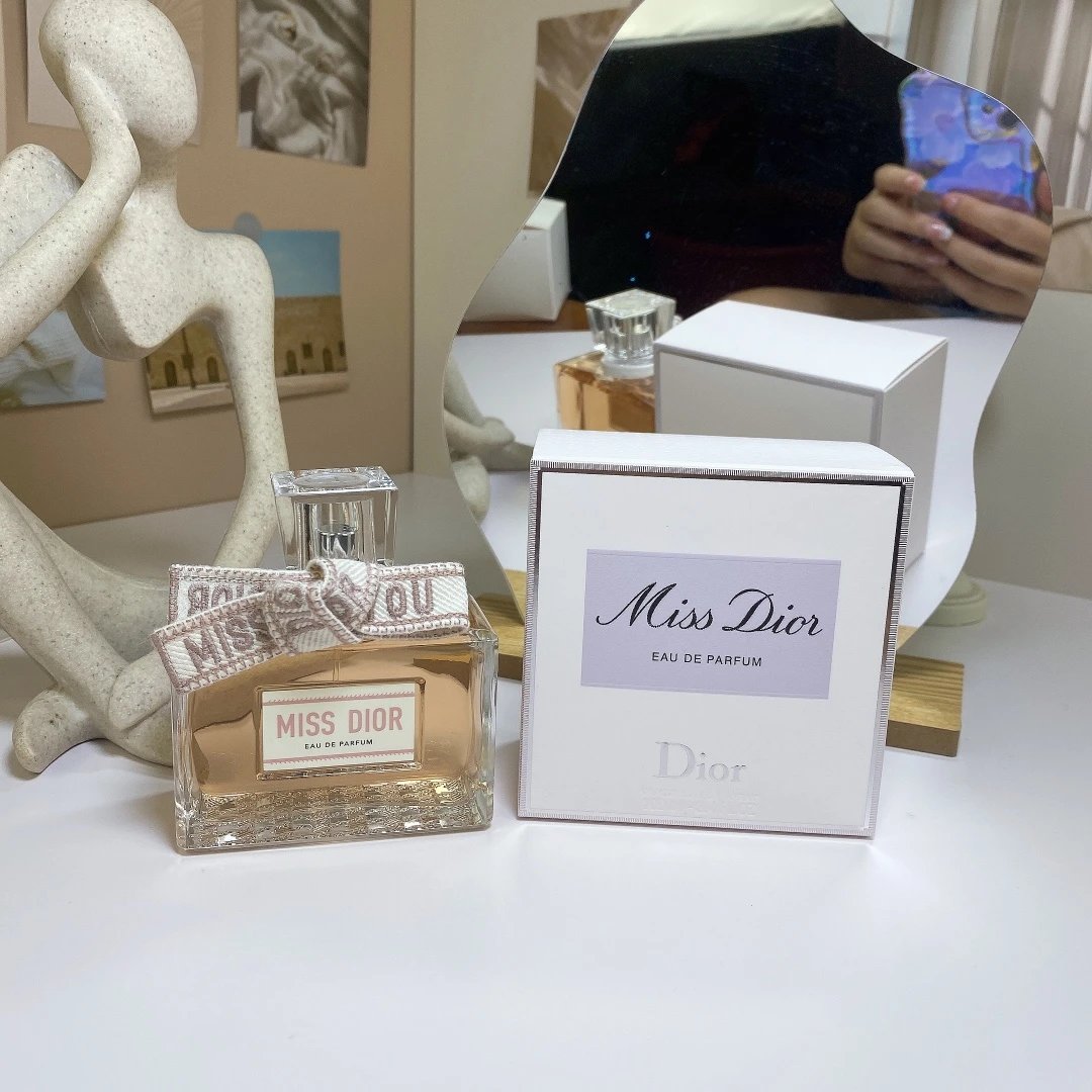 Miss Dior perfume bottle and packaging on a table with a decorative statue in the background.