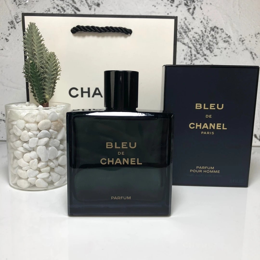 Bleu de Chanel perfume bottle and packaging on a white surface with a decorative plant.
